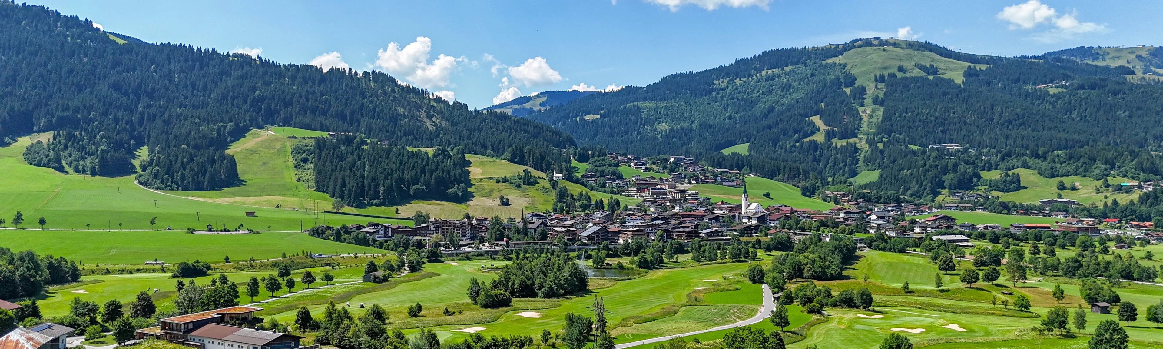 Luftaufnahme: Blick über Wiesen und Golfplatz ins Tal nach Ellmau