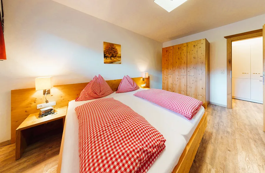 Schlafzimmer im Appartement Ellmauer Halt mit Doppelbett und rot-karierter Bettwäsche